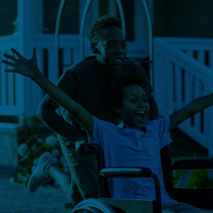 One child pushes another who is in a wheelchair and holds their arms out with joy.