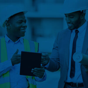 Two men in construction hats looking at documents on a tablet.