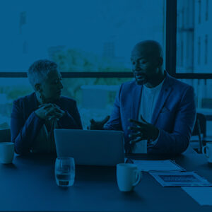 Man and a woman sitting at an office conference table discussing information on a laptop.