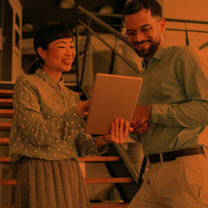 A woman and man review information on a shared tablet in an office.