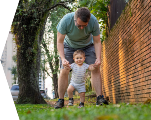 Man helping his toddler walk down a neighborhood street