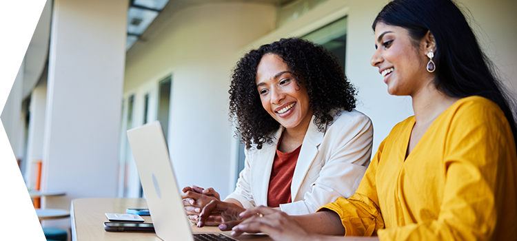 Two women in and office smile at a shared computer screen.
